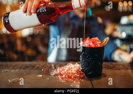 Barman mâle verse dans la boisson rouge verre noir pleine de glace. Emploi barman barman de l'occupation, Banque D'Images