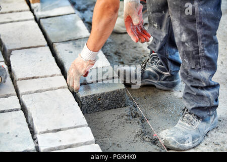 Un ouvrier a les mains gantées utiliser un marteau pour placer les pavés en pierre. La création d'un travailleur à l'aide de blocs et de la chaussée pavée de pierres de granit. Je travailleur industriel Banque D'Images