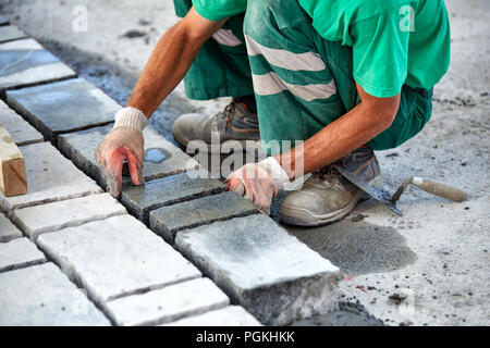 Un ouvrier a les mains gantées utiliser un marteau pour placer les pavés en pierre. La création d'un travailleur à l'aide de blocs et de la chaussée pavée de pierres de granit. Je travailleur industriel Banque D'Images
