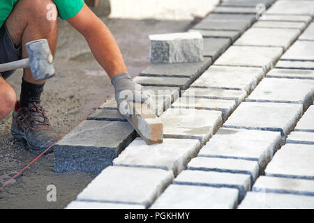 Un ouvrier a les mains gantées utiliser un marteau pour placer les pavés en pierre. La création d'un travailleur à l'aide de blocs et de la chaussée pavée de pierres de granit. Je travailleur industriel Banque D'Images