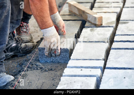 Un ouvrier a les mains gantées utiliser un marteau pour placer les pavés en pierre. La création d'un travailleur à l'aide de blocs et de la chaussée pavée de pierres de granit. Je travailleur industriel Banque D'Images