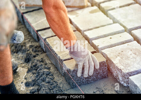 Un ouvrier a les mains gantées utiliser un marteau pour placer les pavés en pierre. La création d'un travailleur à l'aide de blocs et de la chaussée pavée de pierres de granit. Je travailleur industriel Banque D'Images