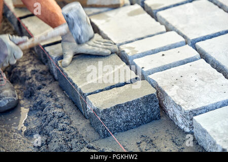 Un ouvrier a les mains gantées utiliser un marteau pour placer les pavés en pierre. La création d'un travailleur à l'aide de blocs et de la chaussée pavée de pierres de granit. Je travailleur industriel Banque D'Images