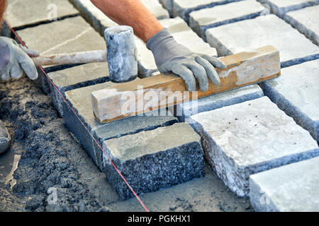 Un ouvrier a les mains gantées utiliser un marteau pour placer les pavés en pierre. La création d'un travailleur à l'aide de blocs et de la chaussée pavée de pierres de granit. Je travailleur industriel Banque D'Images