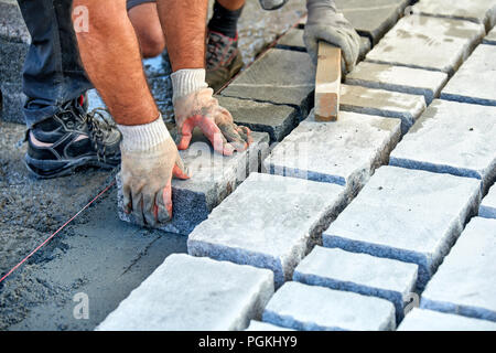 Un ouvrier a les mains gantées utiliser un marteau pour placer les pavés en pierre. La création d'un travailleur à l'aide de blocs et de la chaussée pavée de pierres de granit. Je travailleur industriel Banque D'Images