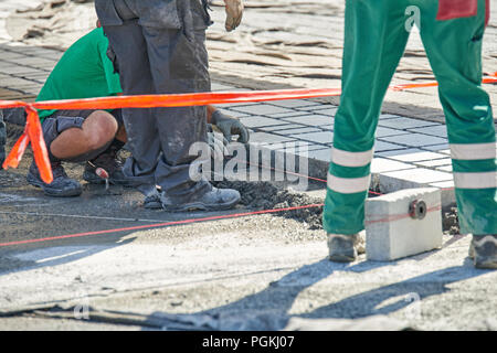 Un ouvrier a les mains gantées utiliser un marteau pour placer les pavés en pierre. La création d'un travailleur à l'aide de blocs et de la chaussée pavée de pierres de granit. Je travailleur industriel Banque D'Images