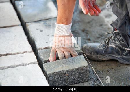 Un ouvrier a les mains gantées utiliser un marteau pour placer les pavés en pierre. La création d'un travailleur à l'aide de blocs et de la chaussée pavée de pierres de granit. Je travailleur industriel Banque D'Images
