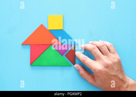 Man's hand pointing at maison faite à partir de casse-tête tangram sur table en bois Banque D'Images