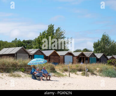 Un couple assis sous un parapluie à côté des cabines de plage sur la plage de Studland Bay, sur la côte jurassique, Dorset, UK Banque D'Images