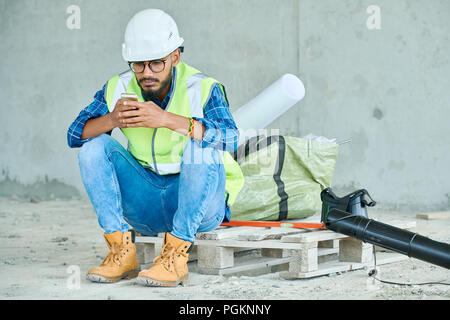 Portrait du travailleur de la construction à l'aide du Moyen-Orient tout en tenant smartphone pause du travail sur place, copy space Banque D'Images