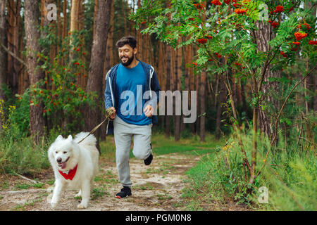 Homme barbu portant costume sport courir avec le chien dans la forêt Banque D'Images