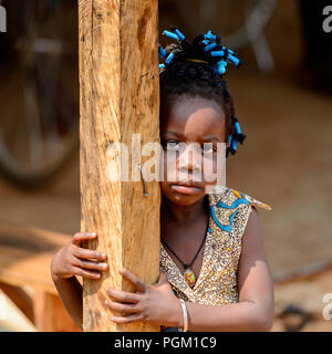 PIRA, BÉNIN - Jan 12, 2017 : petite fille béninois non identifiés avec tresses en vêtements colorés se cache derrière le poteau en bois. Bénin enfants souffrent de po Banque D'Images