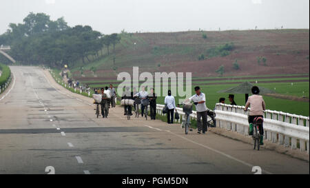 Les travailleurs à pied ou pousser les vélos le long d'un vide sans circulation l'autoroute près de Pyongyang, en Corée du Nord Banque D'Images