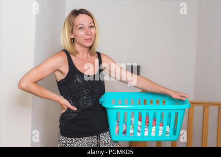 Jeune femme à faire des travaux ménagers tenant un panier de blanchisserie Banque D'Images