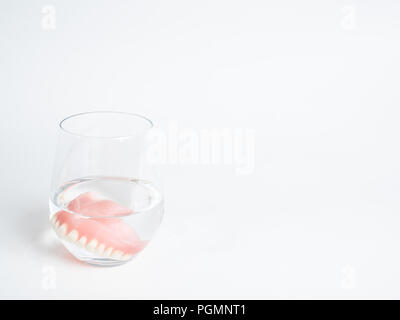 Un ensemble de dentier dans un verre d'eau sur un fond blanc Banque D'Images