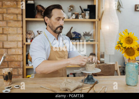 Dark-haired sentiment potter barbu occupé à travailler avec roue de poterie Banque D'Images