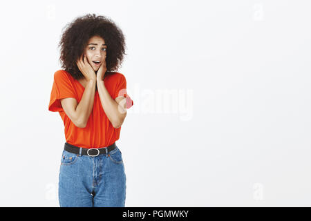 Tourné à l'intérieur de bien timides african american woman with afro coiffure, d'avoir peur et tendre, se tenant la main sur le visage et crier de peur, tremblant plus personne debout sur fond gris Banque D'Images