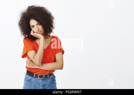 Jeune fille ne peut pas rester plate parle. Déplut assez jolie femme avec coupe afro sur la tête penchée, palm, fronçant et bouder de déplaisir, indifférent et dérangés sur mur gris Banque D'Images