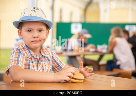 Garçon enfant préscolaire mange hamburger assis dans les jardins d'cafe,Cute happy boy eating hamburger assis dans le restaurant, manger de délicieux sain de l'enfant accueil Banque D'Images