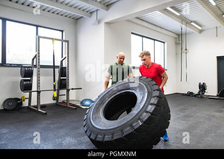 Mettre en place jeune homme avec un entraîneur personnel dans la salle de sport de l'exercice, déplacer des pneu. Banque D'Images