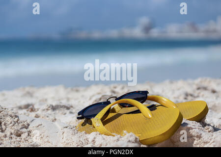 Aperçu de l'été. Tongs et lunettes de soleil dans le sable. Se concentrer sur les détails de santal. Mer des Caraïbes, dans l'arrière-plan. Banque D'Images