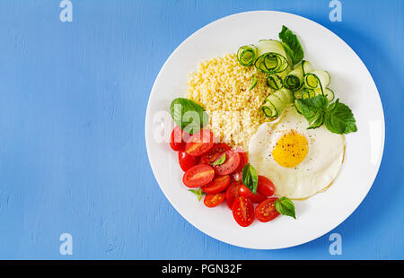 Petit déjeuner sain. Menu diététique. Porridge de millet et de tomates, salade de concombre et d'œufs au plat. Vue d'en haut. Mise à plat Banque D'Images