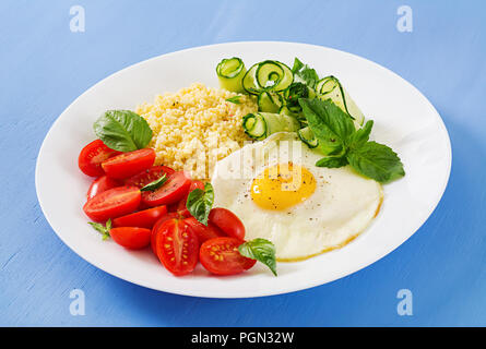 Petit déjeuner sain. Menu diététique. Porridge de millet et de tomates, salade de concombre et d'œufs au plat. Banque D'Images