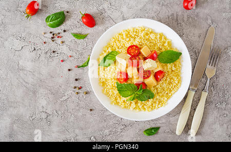 Bouillie de mil avec le fromage, le beurre et le basilic dans un bol blanc. La nourriture bonne. Le petit-déjeuner. Vue d'en haut. Mise à plat Banque D'Images