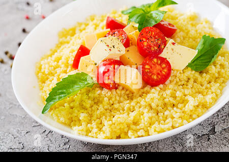 Bouillie de mil avec le fromage, le beurre et le basilic dans un bol blanc. La nourriture bonne. Le petit-déjeuner. Banque D'Images