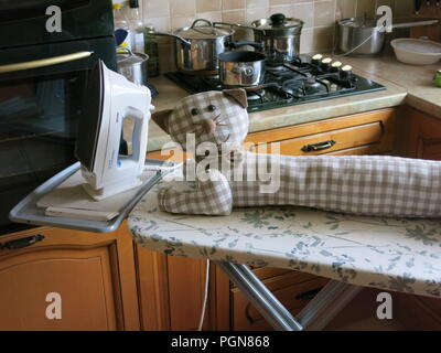 Cuisine domestique avec un jouet chat peluche fabriqués à partir de tissu vichy, allongé sur la table à repasser Banque D'Images