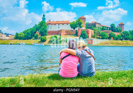 Le jeune couple s'asseoir sur la rive de la rivière Vistule donnant sur le château de Wawel, Cracovie, Pologne Banque D'Images