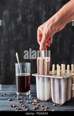 La main de la jeune fille prend de la moisissure, des produits naturels faits à la crème glacée sur un bâton sur une table en bois noir avec un espace réservé au texte Banque D'Images
