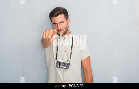 Beau jeune homme plus mur gris grunge holding vintage photo caméra pointant avec le doigt à la caméra et à la main, vous signe, positif et confiant Banque D'Images