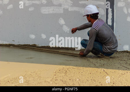 Travailleur de la maçonnerie est à l'aide d'une truelle à lisser ou long plancher concret de mise à niveau de l'étape de travail de la construction du bâtiment. Banque D'Images