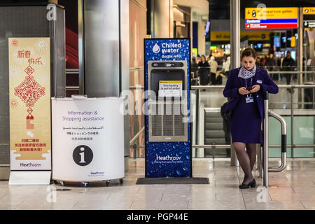 L'aéroport de Heathrow, Londres, ROYAUME UNI - 28 janvier 2018 - un travailleur de l'aéroport se penche sur son smartphone debout à côté d'un poste de remplissage d'une bouteille d'eau Banque D'Images