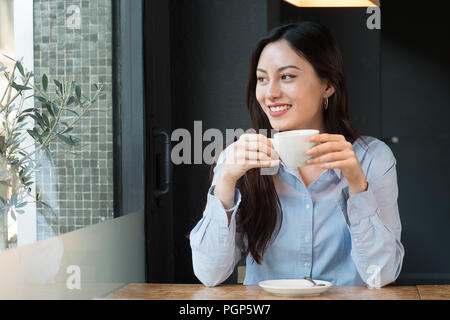 Jolie femme de boire du café en regardant par la fenêtre Banque D'Images