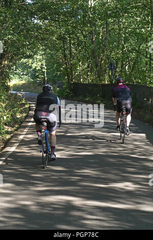 Vu de l'arrière 2 hommes sur push up vélo Vélos une colline escarpée lane près de Bradfield, Sheffield, Yorkshire, Angleterre Banque D'Images