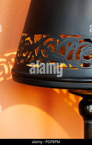 Décor marocain. Black metal percé l'ombre lampe jette une ombre sur un modèle orange wall. Close up detail. Lieu : Marrakech, Maroc Banque D'Images