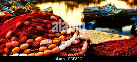 Au bord Maroc close up au coucher du soleil de filets de pêche rouge, orange, bleu flotte bateaux. Couleur de l'eau par l'or du soleil couchant. Lieu : Essaouira Banque D'Images