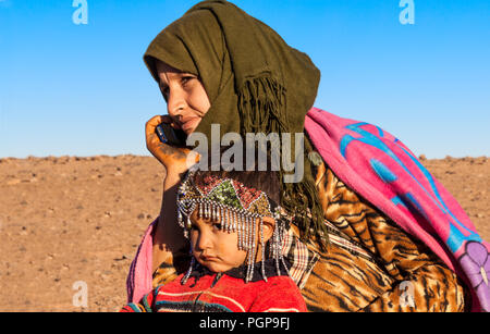 Enfant nomade et la mère sur un téléphone cellulaire dans la région de Maider du désert du Sahara au Maroc le 28 décembre 2012. Les nomades font paître leur bétail. Banque D'Images