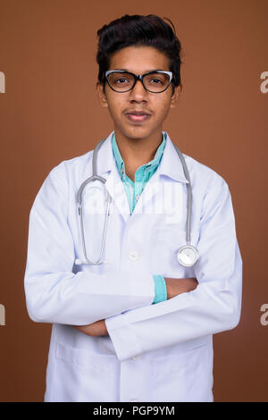 Jeune garçon indien médecin portant des lunettes contre brown background Banque D'Images