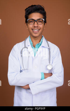 Jeune garçon indien médecin portant des lunettes contre brown background Banque D'Images