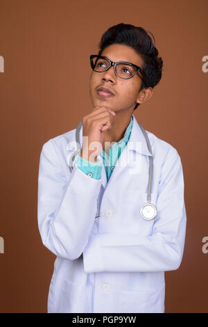 Jeune garçon indien médecin portant des lunettes contre brown background Banque D'Images