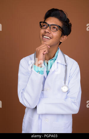 Jeune garçon indien médecin portant des lunettes contre brown background Banque D'Images