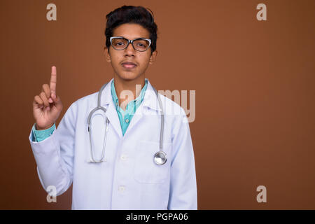 Jeune garçon indien médecin portant des lunettes contre brown background Banque D'Images