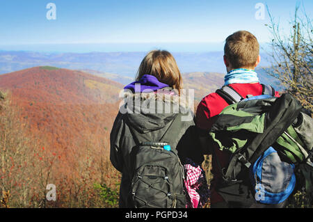 Jeune femme et homme debout avec le dos tourné, à la chaîne de montagnes à couvert de rouge, orange, jaune sous la forêt de feuillus sans nuages bleu s Banque D'Images