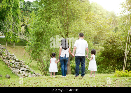 La famille asiatique à l'extérieur. Les parents et les enfants se tenant la main et marcher au parc. Vue arrière. Banque D'Images