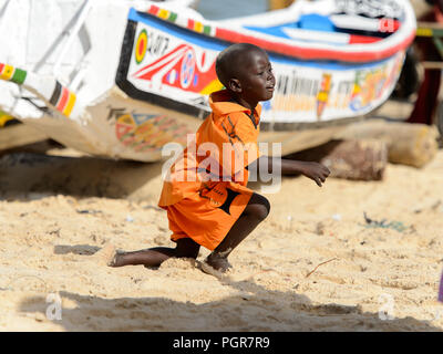 KAYAR, SÉNÉGAL - AVR 27, 2017 : petit garçon sénégalais non identifiés en costume orange joue sur la côte de l'océan Atlantique. De nombreuses personnes travaillent dans Kayar p Banque D'Images