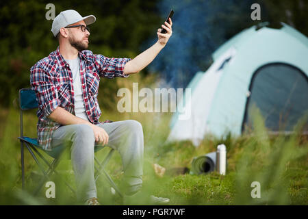 Jeune homme assis sur une chaise et attraper la connexion de son téléphone portable dans le camp Banque D'Images