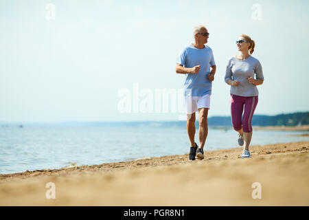Senior homme et femme fonctionnant en bas de sable avec l'arrière-plan sur l'eau Banque D'Images